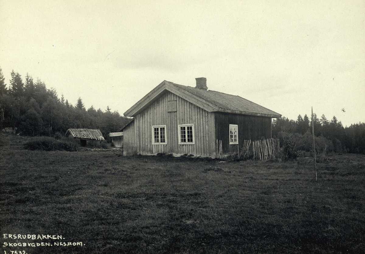 Ersrudbakken, Skogbygda, Nes, Øvre Romerike, Akershus. Lita stue med uthus i bakgrunnen sett fra jorde.