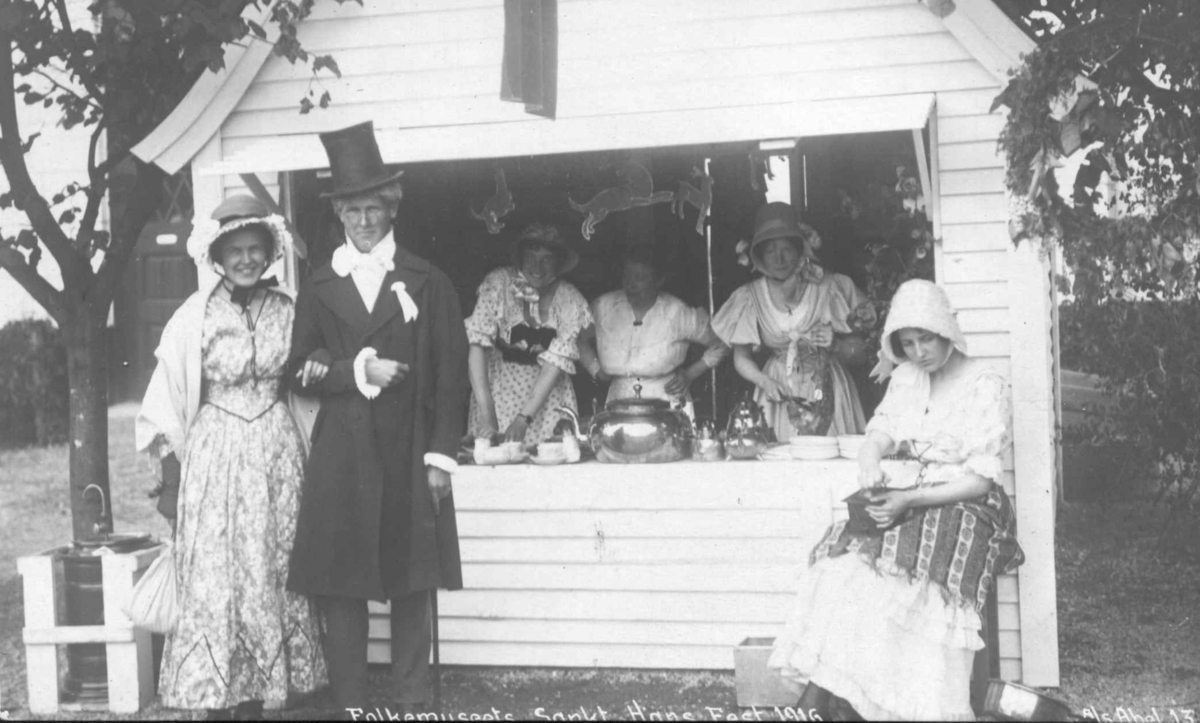 St. Hans fest på Norsk Folkemuseum i 1916. Mann og kvinner med hatter foran salgsbod.
