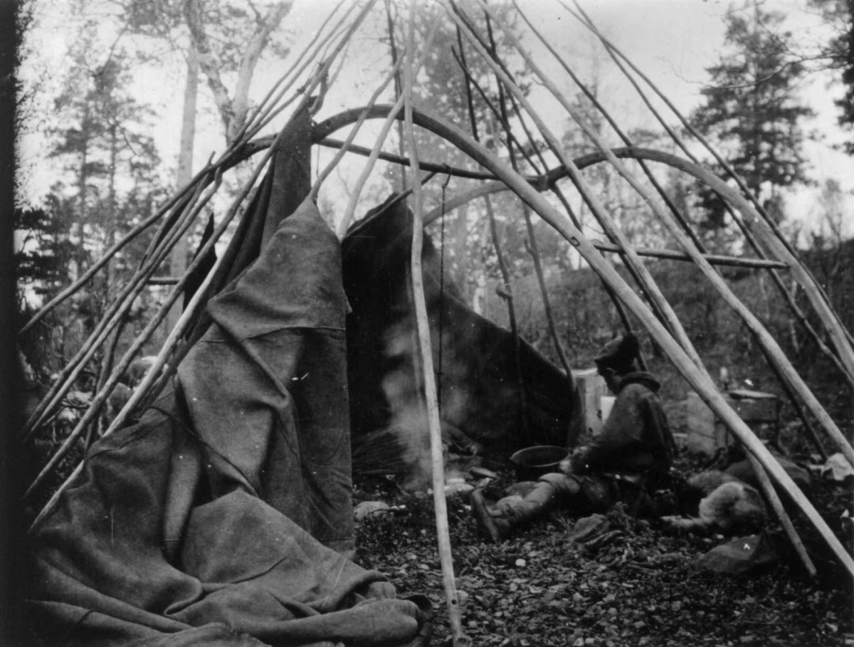 Sameleir like før avreisen, kun reisverket til teltet står igjen med noe av teltduken. En person sitter ved kokestet. Fosshaug høsten 1914.