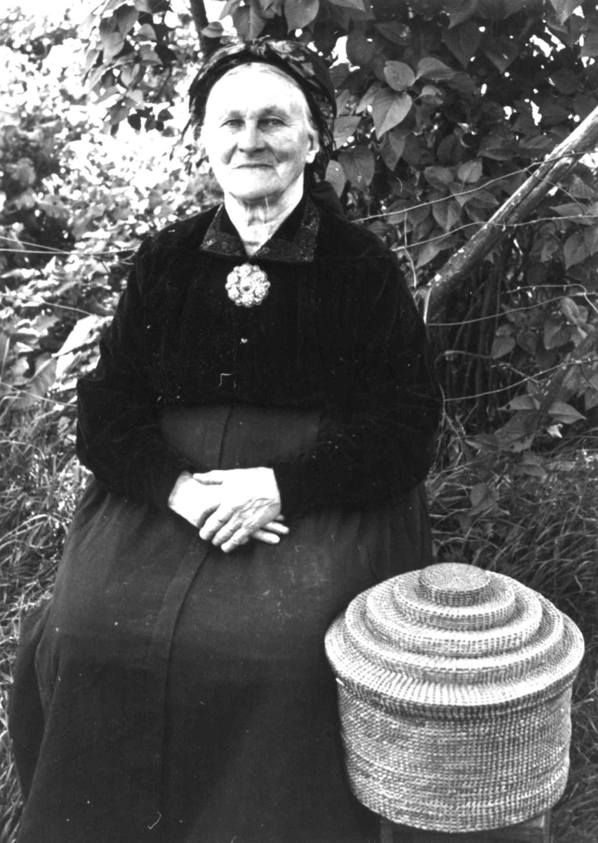 Dølemo Åmli, Aust-Agder 1940. Fru Sigrid Dølemo sitter ved siden av en kurv til å ha silketørklær og sølv i. 