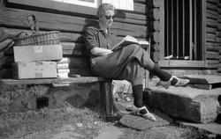 Dordi Arentz sitter utenfor en hytta og leser.  Fotografert 