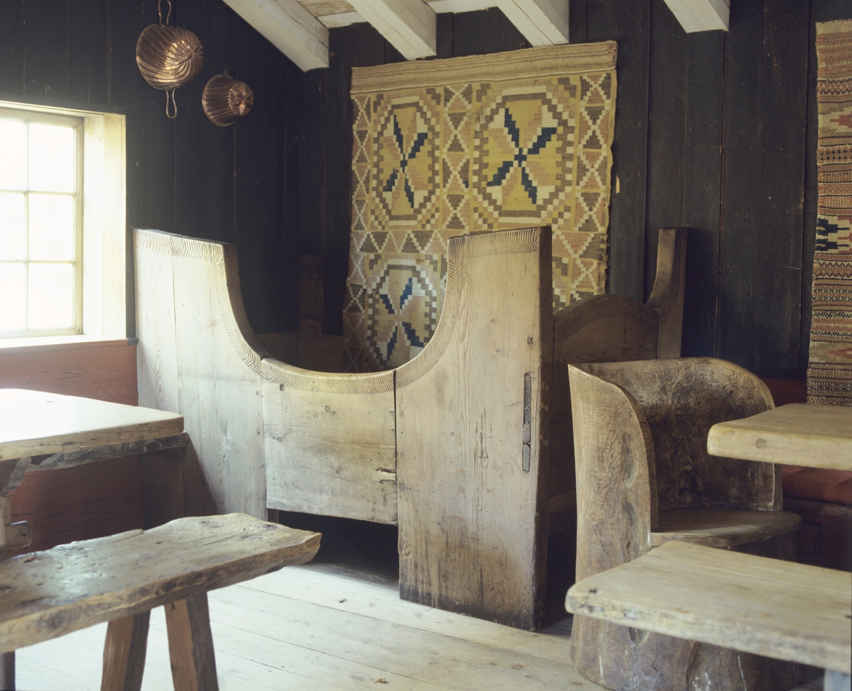 Middelaldermøblement med et åkle på veggen, kubbestol og benker ved bordet.  llustrasjonsbilde fra Bonytt 1986.
