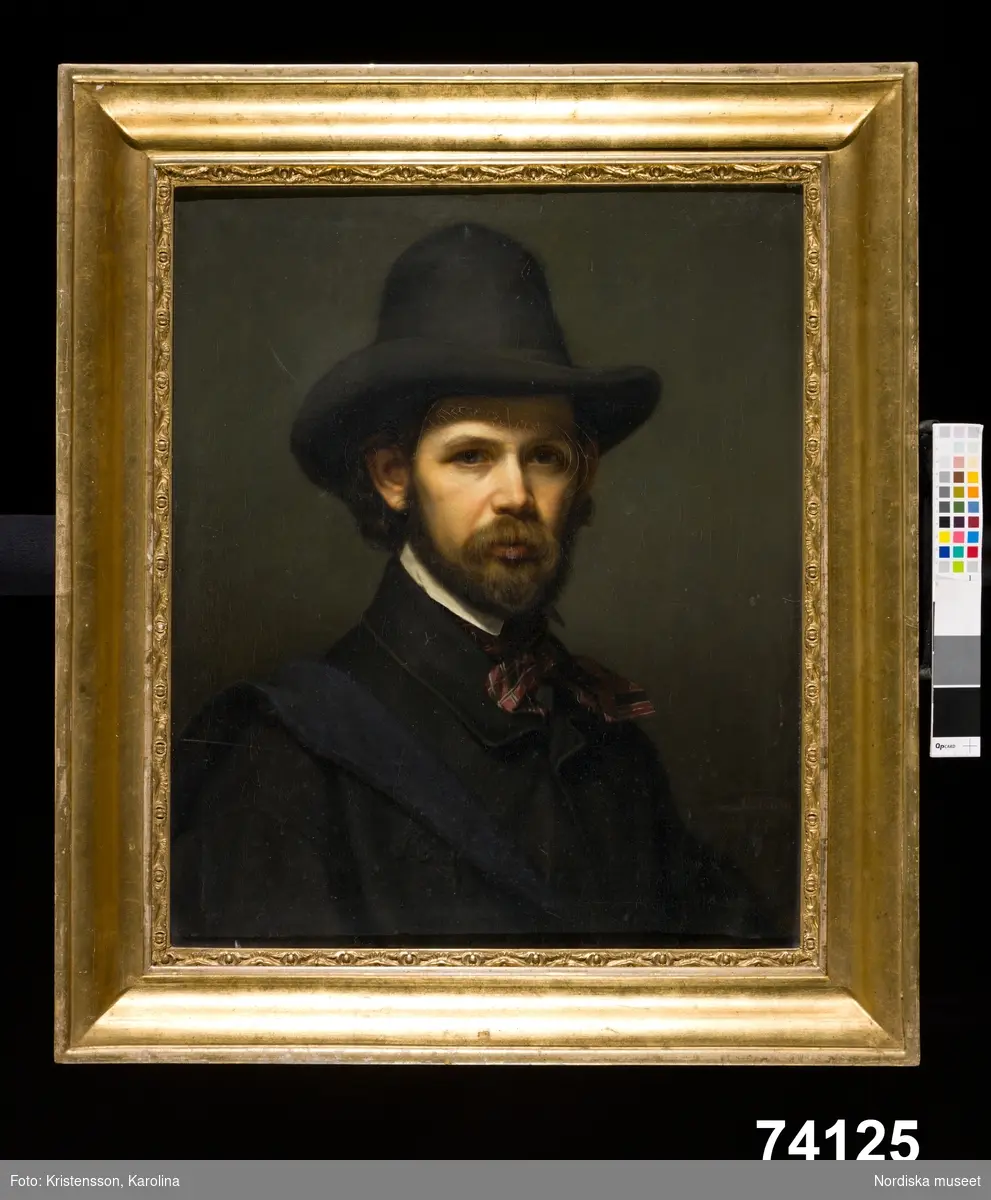 Herrporträtt, bröstbild, närmast en face. Mustasch och skägg, iförd hatt och mörk rock.
