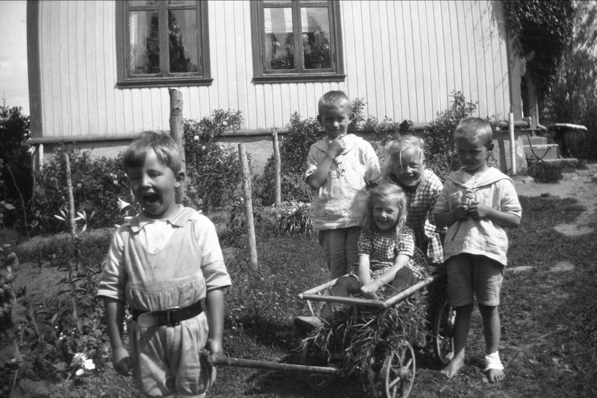 Barn leker med en vogn foran et hus. Robsahm og Lund.