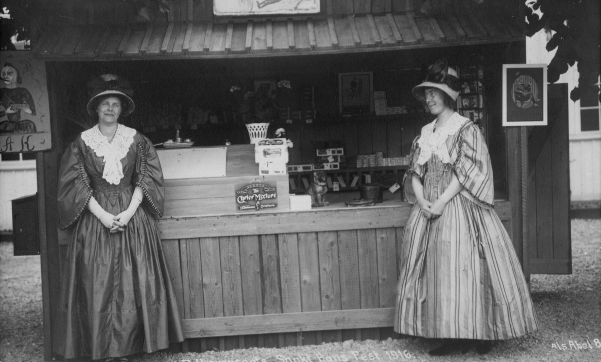 Postkort. Kvinner foran markedsbod hvor det selges tobakk. Norsk Folkemuseums St. Hansfest 1916.