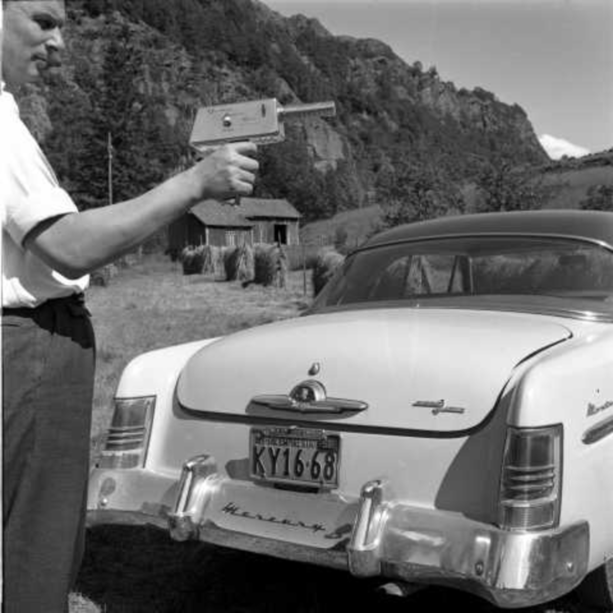 Geigerteller, Sørlandet, 1956.Mann ved bil, hesjer i bakgrunnen.