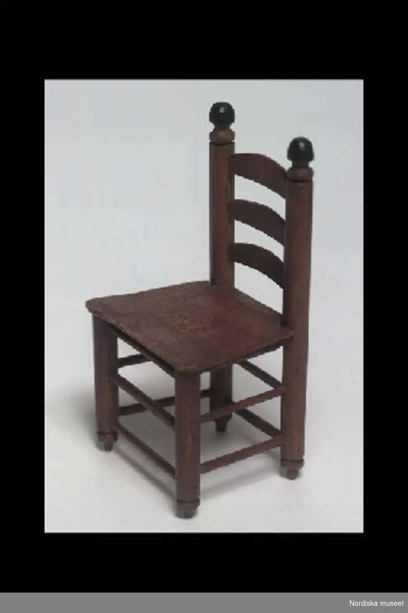 Inventering Sesam 1996-1999:
L  13  cm
Stol, stegstol, leksak, av brunbetsad furu. Rundsvarvade ben och ryggstolpar, tre bågformade horisontala spjälor i ryggen, träsits, tunna träslåar mellan benen. Ryggstoplarna avslutas upptill med svartmålade knoppar.
Stolar av denna modell kallas vanligen stegstol eller gripsholmsstol och var vanliga i Sverige under 1700-talet.
Stolen har tillhört givarens mor Hedda Brusewitz, f Bredberg 1856.
Birgitta Martinius 1997