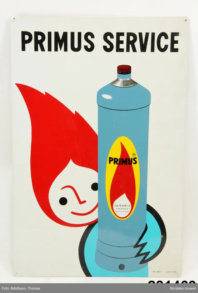 Reklamskylt. Vit med texten "Primus service" högt upp. Därunder en blågrå gasflaska med texten "Primus AB...". Flaskan hålls av en figur med blå hand och kropp och ett stiliserat ansikte som avslutas med hår i form av en röd eldslåga. Fyra hål för montering.

ULHA 2008-03-19 