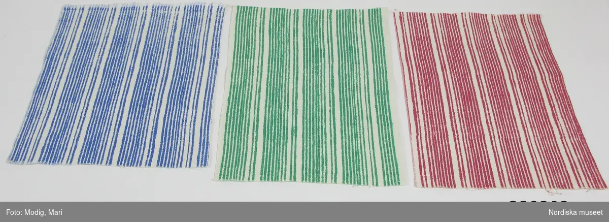 3 tygprover (a-c), på inredningstyg i samma randmönster. Mönstret heter Liljerand, komponerat 1946 av Astrid Sampe för NK:s Textilkammare.
Tryckt på linneliknande väv i cellull s.k. vistra, i en färg mot vit botten.
a) Mellanblå ränder.
b) Klargröna ränder.
c) Rosaröda ränder.
Alla tre proverna har en stadkant. På både det blå och det röda provet finns en färgskarv som visar att det är handtryckt med ram.
Tryckta i filmteknik som var en ny teknikvid 1930-talets mitt som NK:s Textilkammare var tidiga med. Föreståndaren Astrid Sampe beställde först hos Borås Väveri som tryckte och från 1944 samarbetade hon med Ljungbergs tygtryckeri i Floda i Västergötland. Många kända mönsterritare tecknade tryckmönster för NK.
Se vidare: Innez Svensson Tryckta tyger från 30-tal till 80-tal, Liber 1984 sid 20-23.
Proverna ingår i en större samling som alla tycks komma från NK:s Textilkammare och är från 1940-talets mitt. De har sparats av textilkonstnären Mai Wellner som 1944 kom som estnisk flykting till Stockholm där hon redan 1945 fick arbete hos Astrid Sampe på Textilkammaren. Hon stannade till 1946 och proverna borde därför vara från de åren.
/Berit Eldvik 2008-02-05