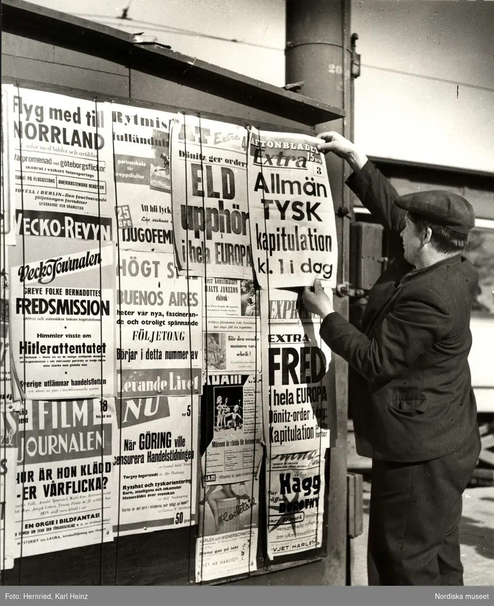 En man hänger upp löpsedlar som annonserar om den tyska kapitulationen och fred i Europa 1945.