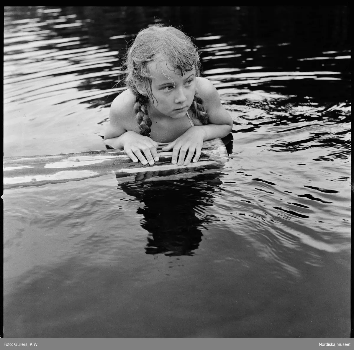 Flicka flyter på stock i vattnet.
