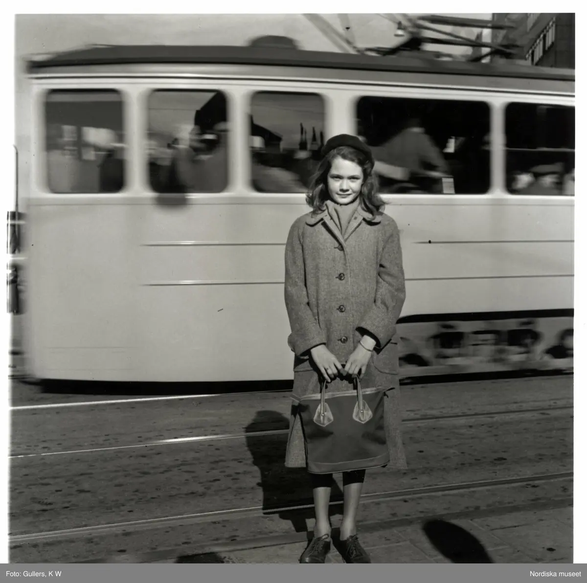 Flicka med v&auml;ska framf&ouml;r sp&aring;rvagn. Norrk&ouml;ping, modereportage f&ouml;r tidningen Vi. 