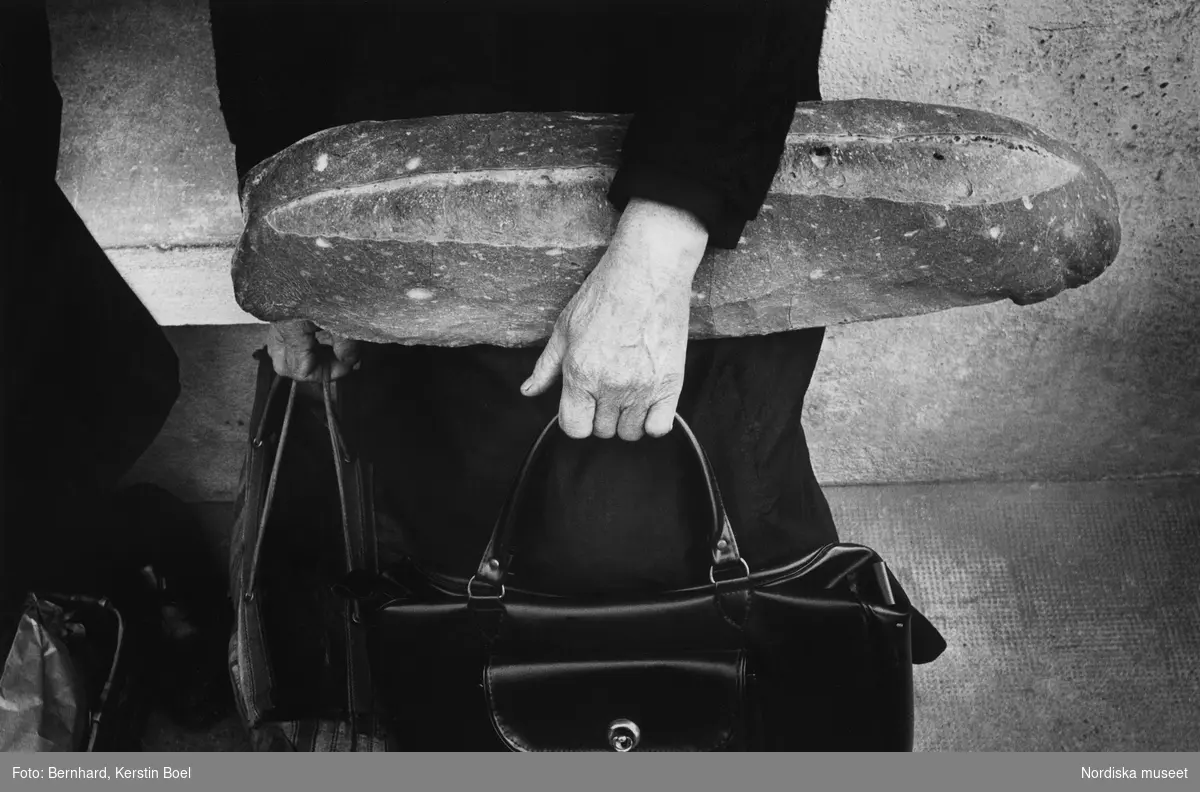 Kvinna som håller i två väskor och ett stort  bröd.