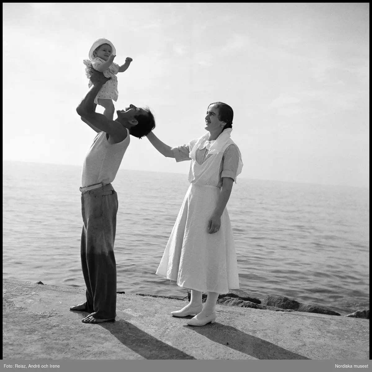 Kvinna och man hållande ett spädbarn på en strand