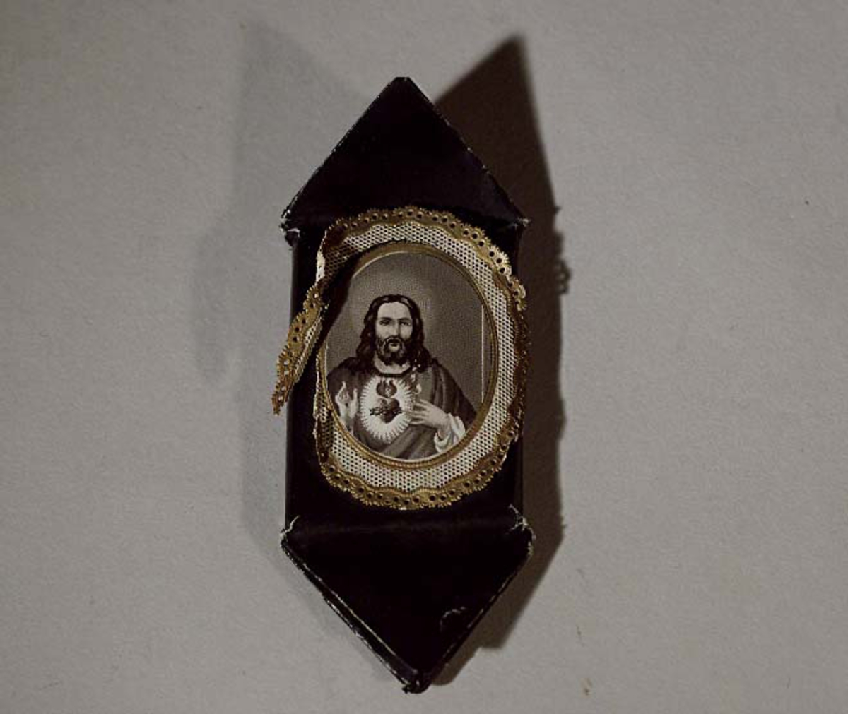 Begravningskaramell, omslag av svart  silkespapper. Svartvit Jesusbild med guldram.