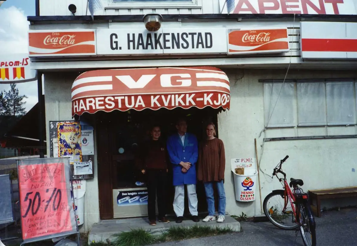 G. Haakenstad landhandel, senere Harestua kvikk-kjøp. Tre personer står utenfor ved inngangsdøra til matbutikken.
