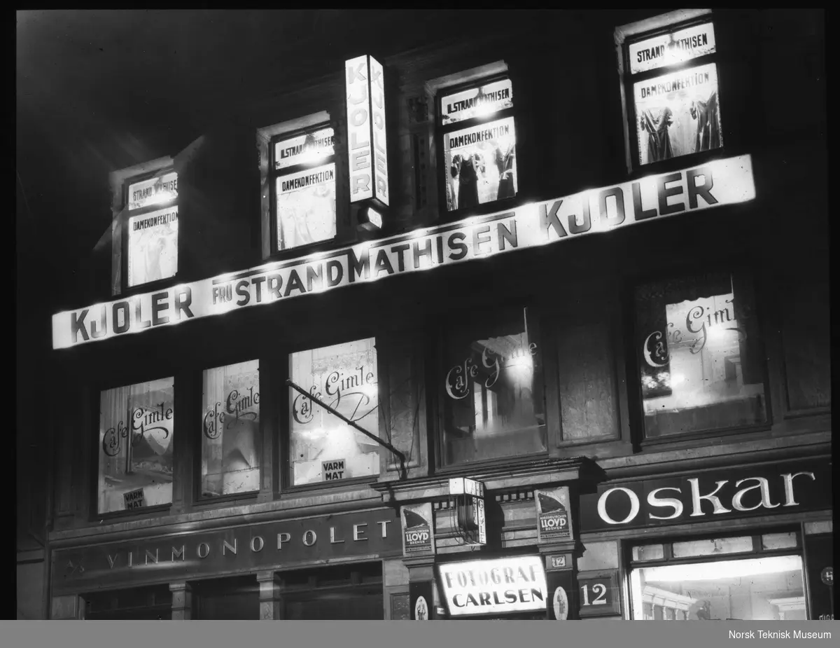 Torvet 12, med blant annet Gimle Café, fasade på bygård i Oslo med opplyste vindusutstillinger og lysreklamer, 1930-tallet