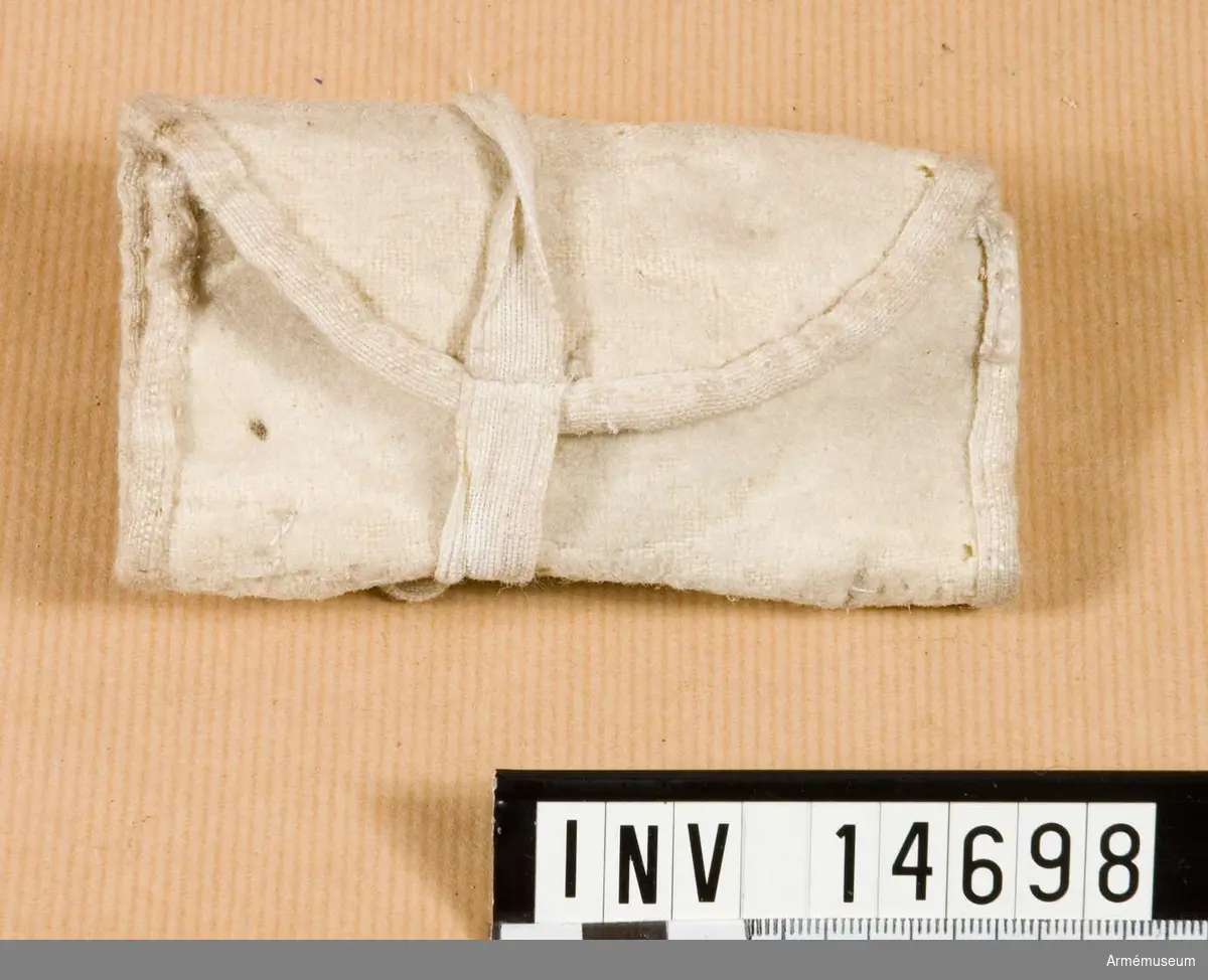 Grupp nr C II.
Samhörande nr är 14697-14707.
Syväska. England. Sysäck av vitt kläde med två fickor för tråd, nålar, knappar och fingerborg (som är av järn). Säcken stänges med två bomullsband.