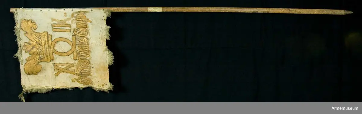 Duk:
Enkel, tillverkad av vit linnelärft. Duken fäst vid stången med en rad tennlickor, delvis ärgade, på ett rött band.

Dekor:
Målat lika på båda sidor Karl XII:s namnchiffer, dubbelt C och på ömse sidor X II, namnchiffret krönes av en öppen, något överdimensionerad krona.

Under detta en inskrift, allt utfört i svartskuggat guld.

Frans:
Rester av gul(?) ullfrans, dubbel.

Stång:
Tillverkad av trä, blågråmålad.