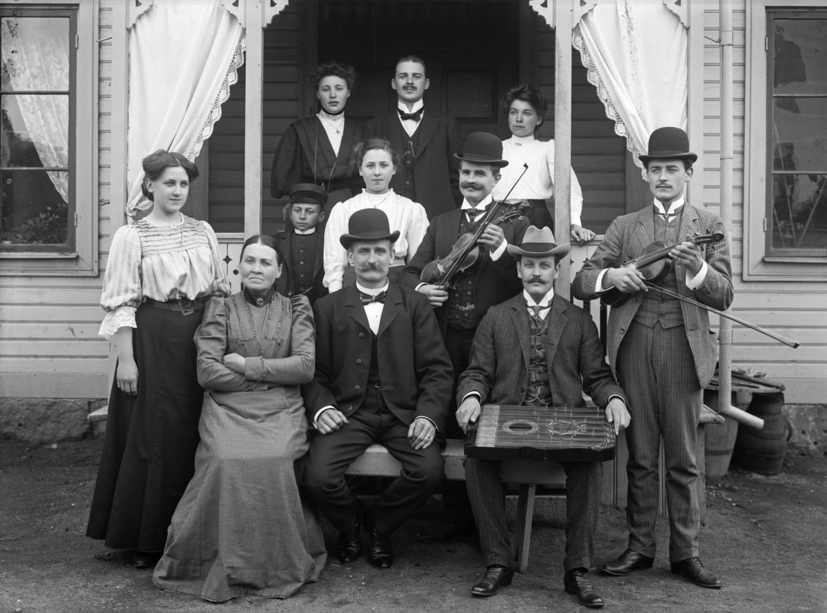 Grupp/familj med musikinstrument framför ett hus, oidentifierad