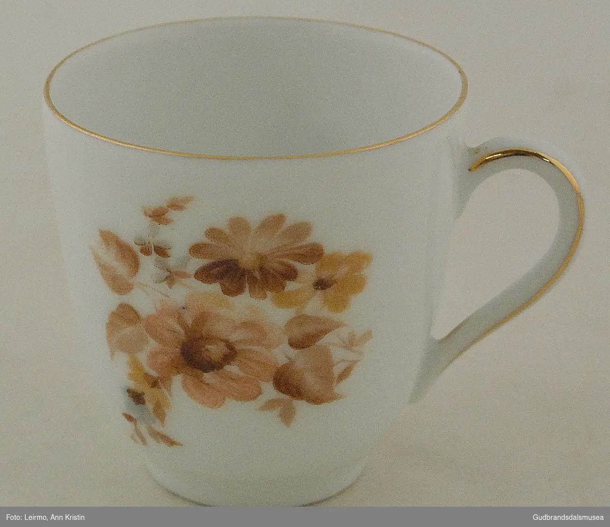 Liten kaffekopp med tilhørende skål. Dekorert med blomstermotiv i bruntoner. Ellers hvit. Pynterand i gullfarge.