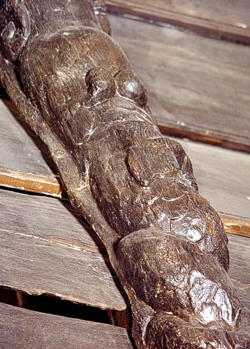 Nereid med uppåtkammad frisyr och hög, välvd panna. På huvudet sitter stora plymliknande bladflikar eller dylikt. Armarna är ersatta med dekorativa bladslingor som även markerar övergången till den fjällförsedda fiskstjärten. Fiskstjärten slingrar sig kring stjärten till en fisk eller en delfin, vars huvud är synligt vid skulpturens fotända.

Bakstycket är kraftigt och snidat i ett med skulpturen. Baksidan är försedd med hak eller urtag. Skulpturens profil är svagt S-formad.
Skulpturen är välbevarad.

Text in English: Nereid with hair combed upward and with high, arched forehead. Plume-like headgear. The arms are replaced by decorative rolled, leafy ornamentation which also marks the transition between the upper and the lower body. The fish tail is entwined with the tail of a fish or dolphin whose head can be seen at the foot of the sculpture.

The backboard is robust and carved in one piece with the figure. The back side of the backboard is carved with hollowed out grooves. The profile is slightly S-shaped.
The sculpture is well preserved.