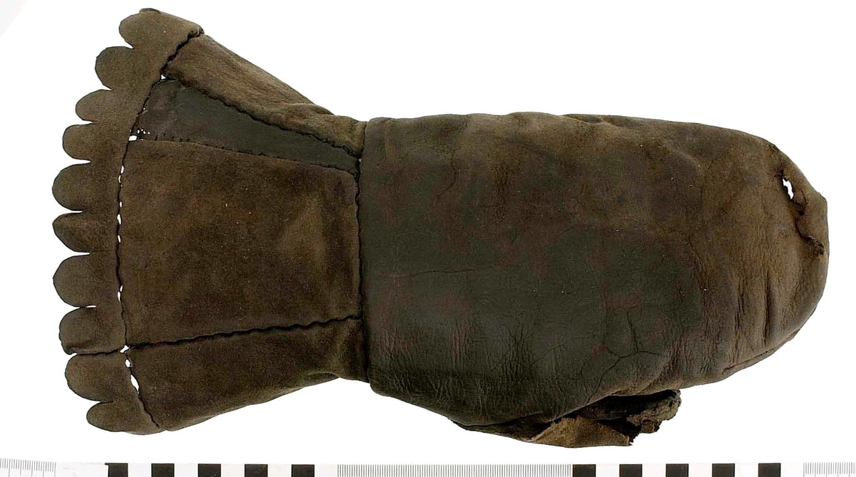 En kragvante till vänster hand. Sydd av flera kraftiga läderstycken. Påsydd bård i ett stycke i form av rundade "tungor" längs kragkanten.