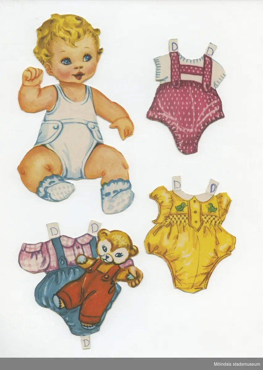 Klippdocka med kläder och tillbehör från 1950-talet. Docka och kläder märkta "Dan" - dockans namn. Dockan, av papp, föreställer en baby, med blont hår, iklädd linne, tygblöja, samt sockar. Garderoben, av papp, består av hängselbyxor med korta ben och tröja, lekdräkt med korta ben, pyjamas, ytterplagg med kapuschong, hakklapp, kloss, samt en fågel. 