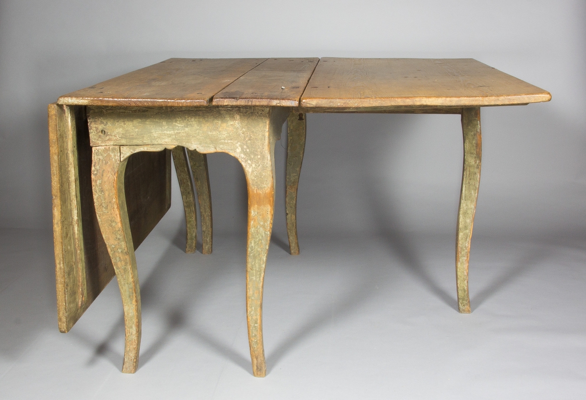 Slagbord i trä, sannolikt furu. Svängda ben, sarg med arbalètedekor. Rektangulär bordsskiva. Dubbla grindar som kan svängas ut och på vilka två större skivor kan vila.