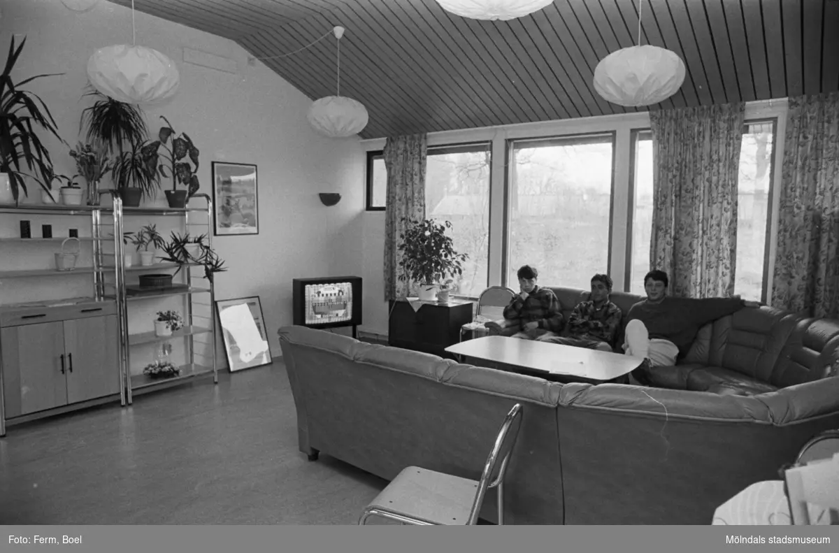 Ett allrum där tre män sitter i en soffa. Dokumentation av Sagåsens flyktingförläggning, 1992.