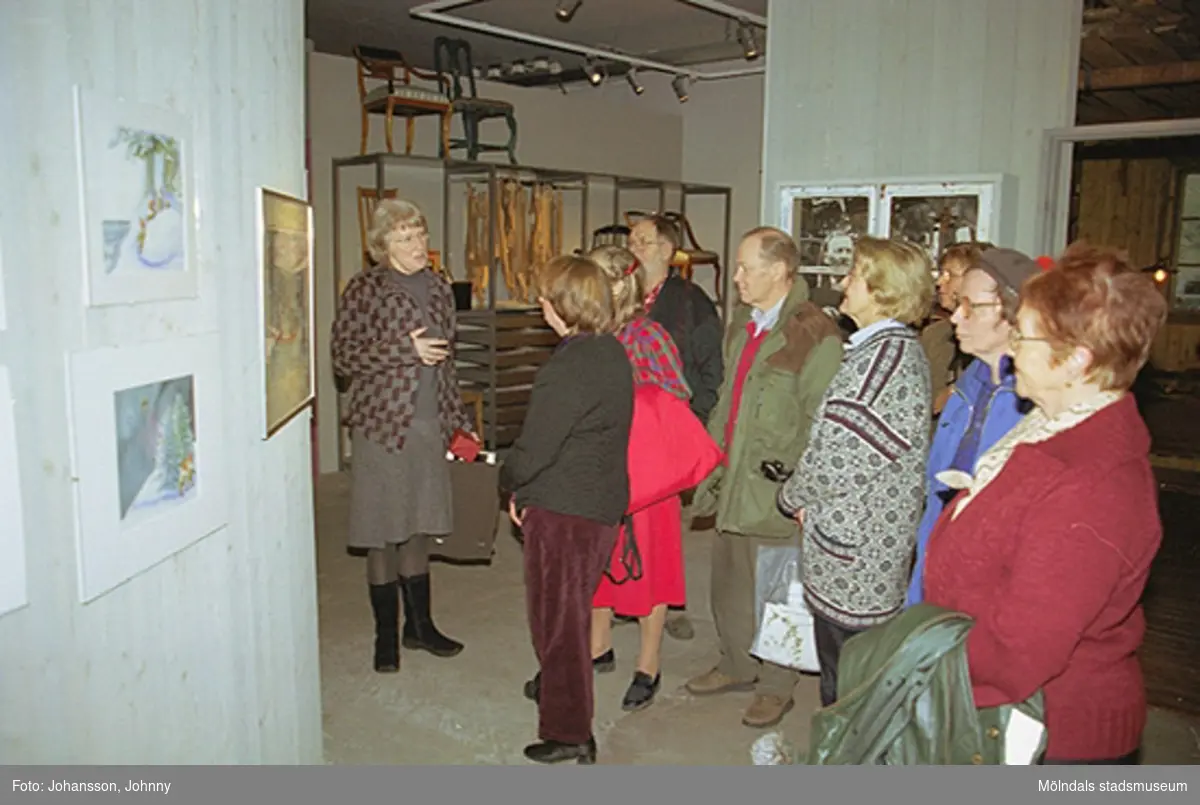 Invigningen på Mölndals museum 2002-11-30.
Museichef Mari-Louise Olsson (mörk överdel och vinröda byxor) tittar på målningar tillsammans med besökare.
Tomteutställningen: 30/11-02 - 1/1-03.