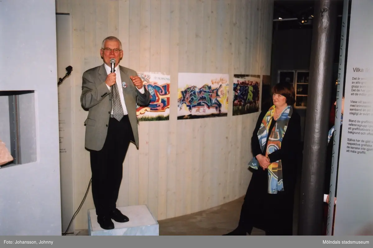 Professor Lars Nordström, ordförande i Västra Götalands Kulturnämnd, håller tal vid invigningen av utställningen "Alltså finns jag" på Mölndals museum, år 2003. Till höger ses museichef Mari-Louise Olsson.