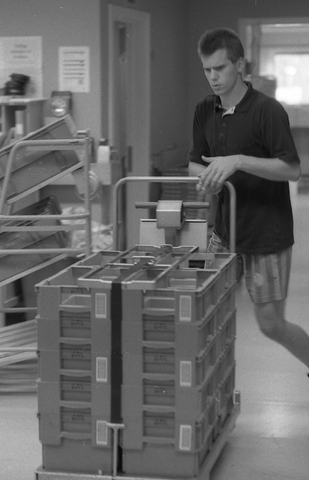 En posttjänsteman fraktar transportlådor på en platåvagn vid
sorteringsavdelningen på en postanstalt. Tillhör en dokumentation av
en lantbrevbärare i trakten av Valdermarsvik av fotograf Ove Kaneberg.