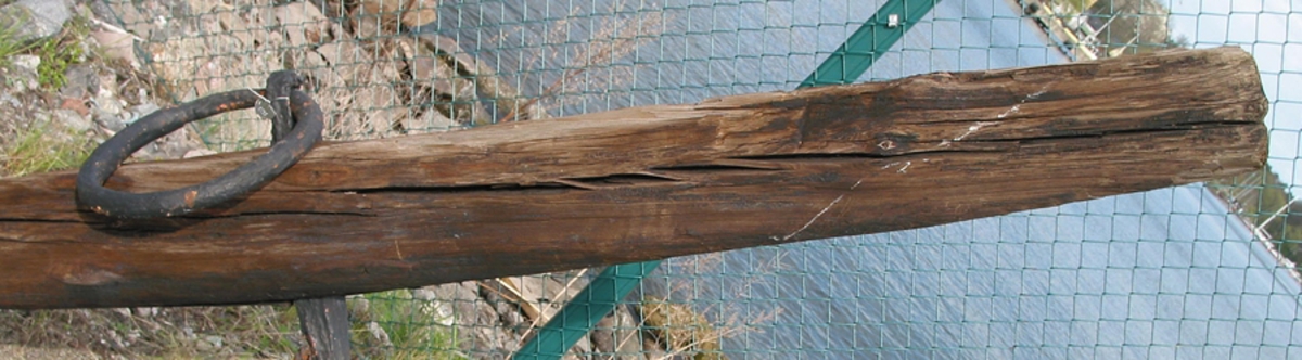 Ankarstock bestående av ett trästycke med urtag mitt på. Ankaret sitter i urtaget och hålls på plats med en modern träplatta.