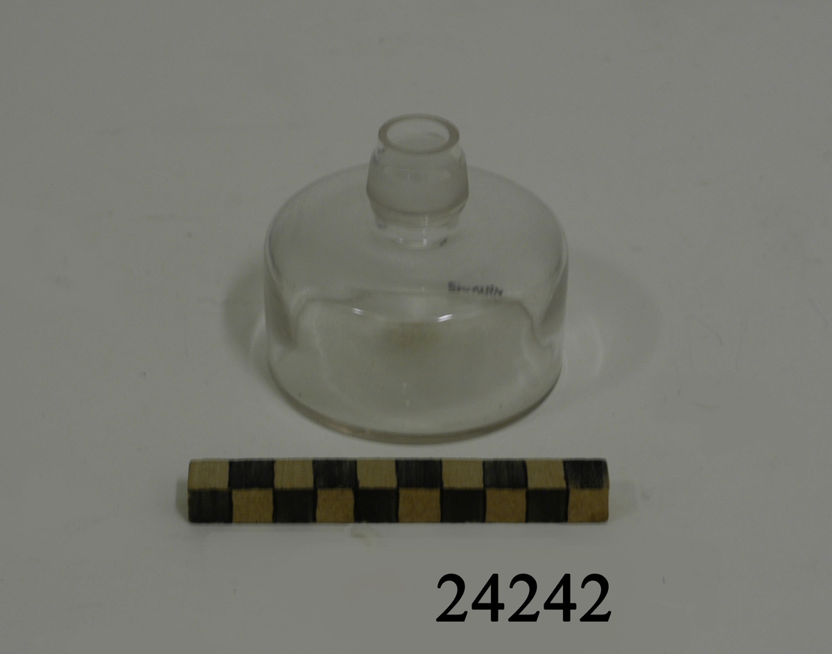 Rund, låg flaska med kort, smal hals av transparant glas. Flaskhalsens metallfäste för veken saknas.