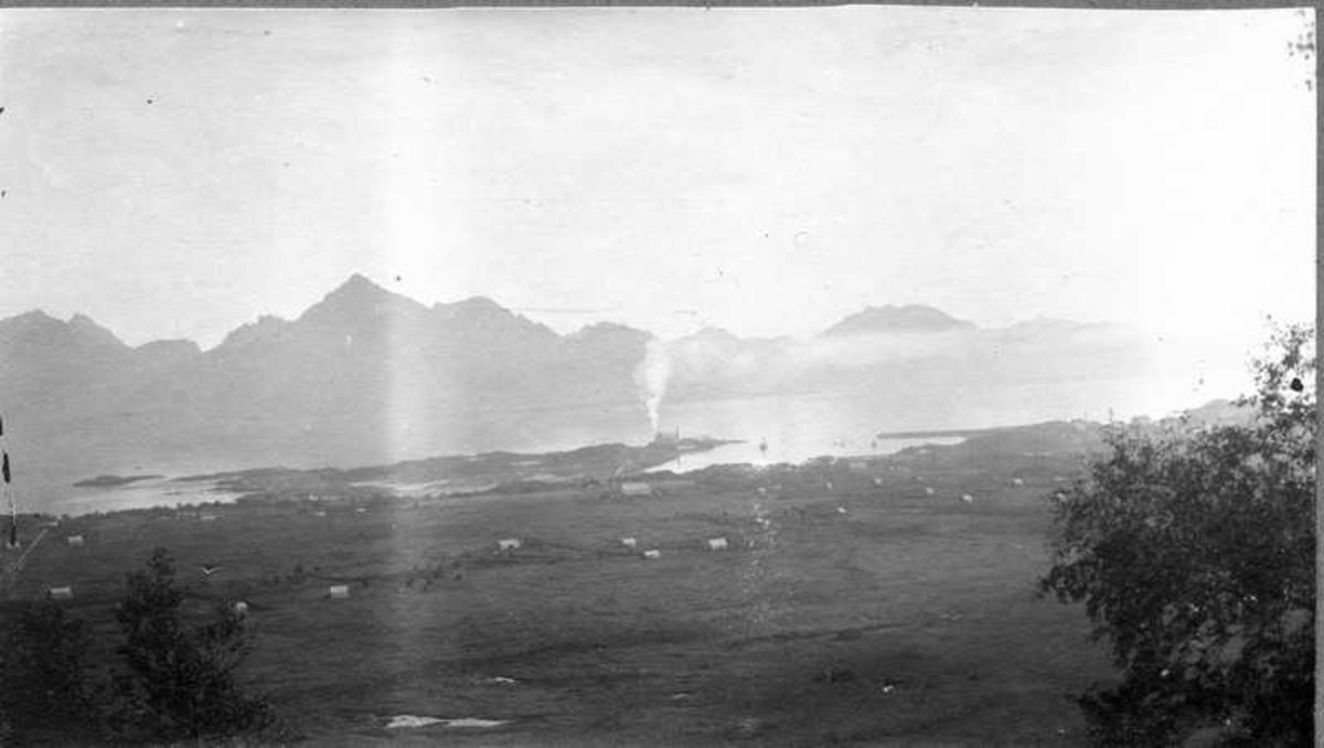 Utsikt over  tettstedet Melbu fra fjellet. Røyk fra produksjonen ved sildoljefabrikken Neptun. 
Bildetekst: "Fra Urvasbrækka."