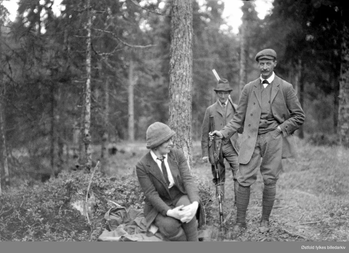 Jaktlag i skogen. Kvinne sitter ved foten av et tre, to menn poserer vedsiden av. Gruppe3.