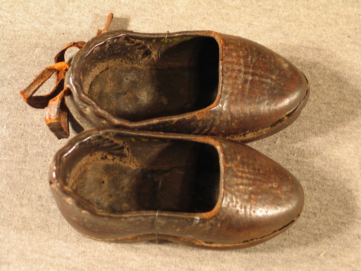 Sydde sko med hardt overlær.
På den eine er det festa to lærband på hælkappa, dei an anten knytast om ankelen eller i sløyfe bak. På den andre skoen er desse vekke.