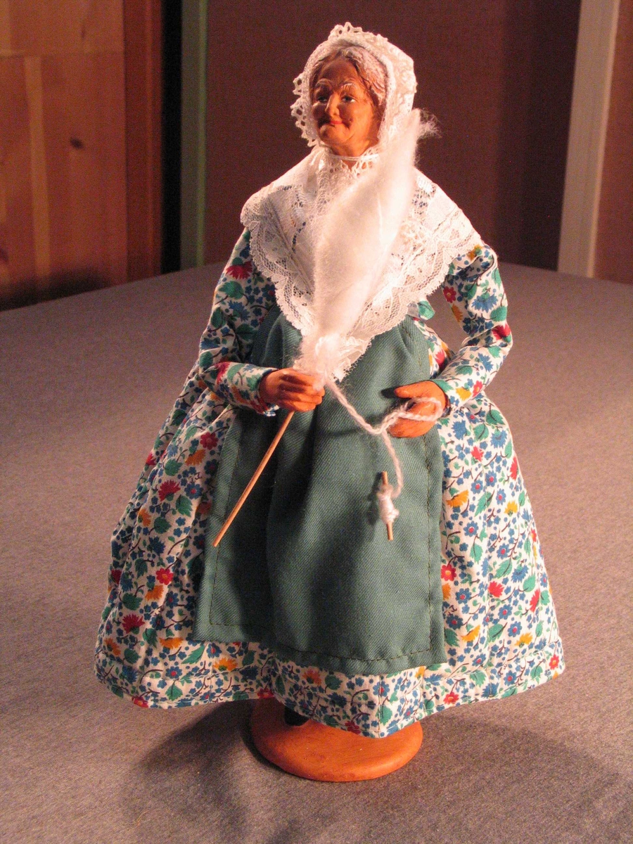 Eldre dame iført tradisjonell kjole m/tilbehøyr. Ho spinn på handtein.