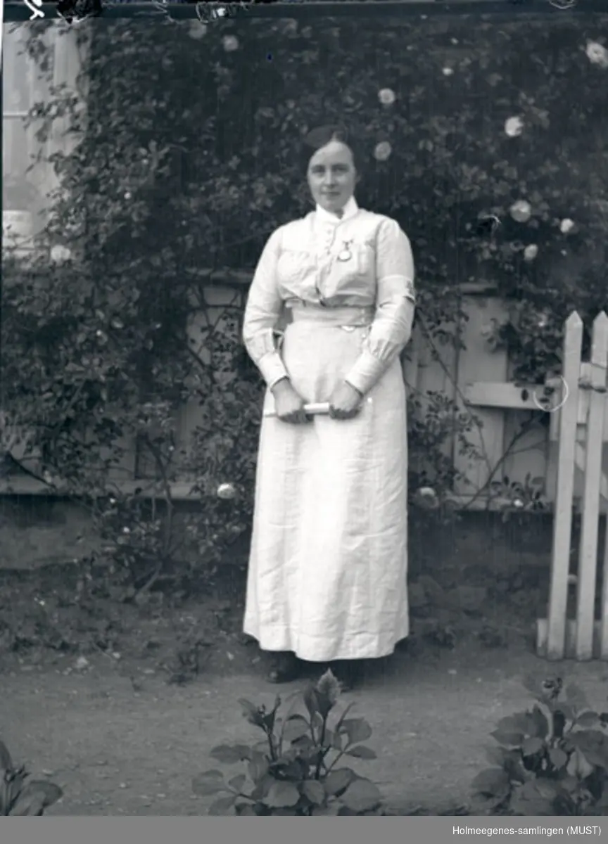En kvinne i en hage. Hun har på seg Norske kvinners sanitetsforenings sykepleieruniform.