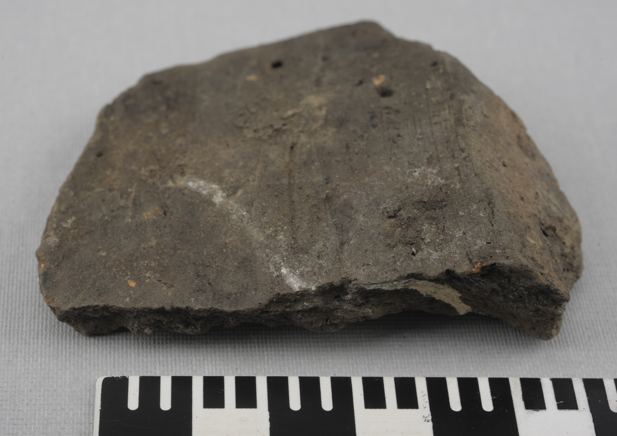 Skår av grå keramikk. Tynnere i den ene ende.