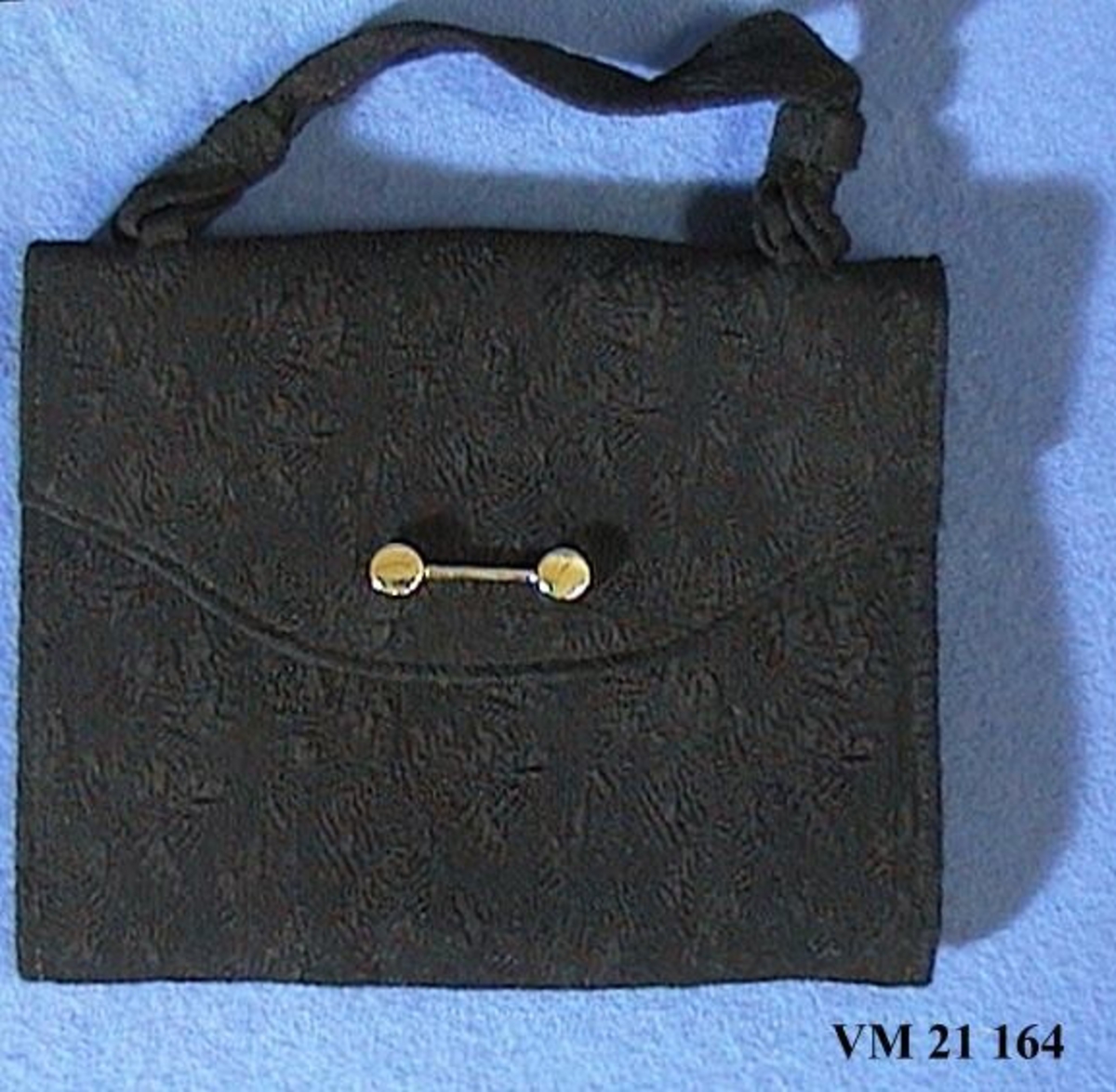 Svart aftonväska med lås i vitmetall. Väskan bäres i ett kort band. Väskans svarta tyg har ett invänt blommönster.