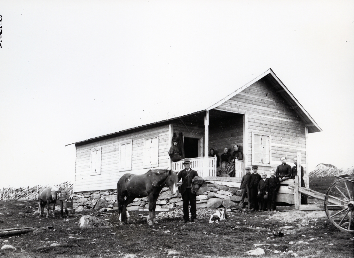 Mennesker samlet utenfor hus, antagelig stølssæl, sammen med hund og to hester