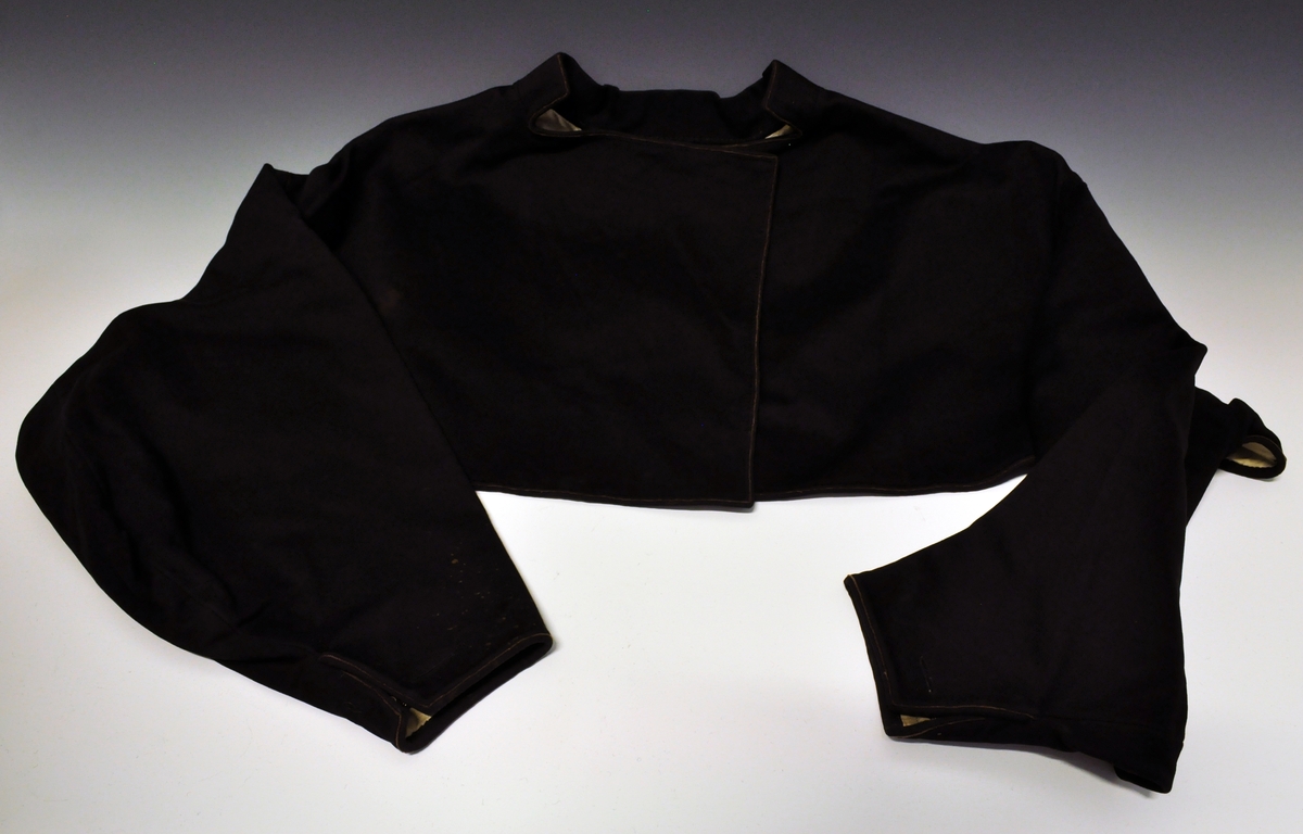 Fra protokoll:Består av:
D: Trøye/jakke  (Slengetrøye) av svart klæde med ei einskild stikka bylgjeline paa kvar erm. Lereftsfôra.