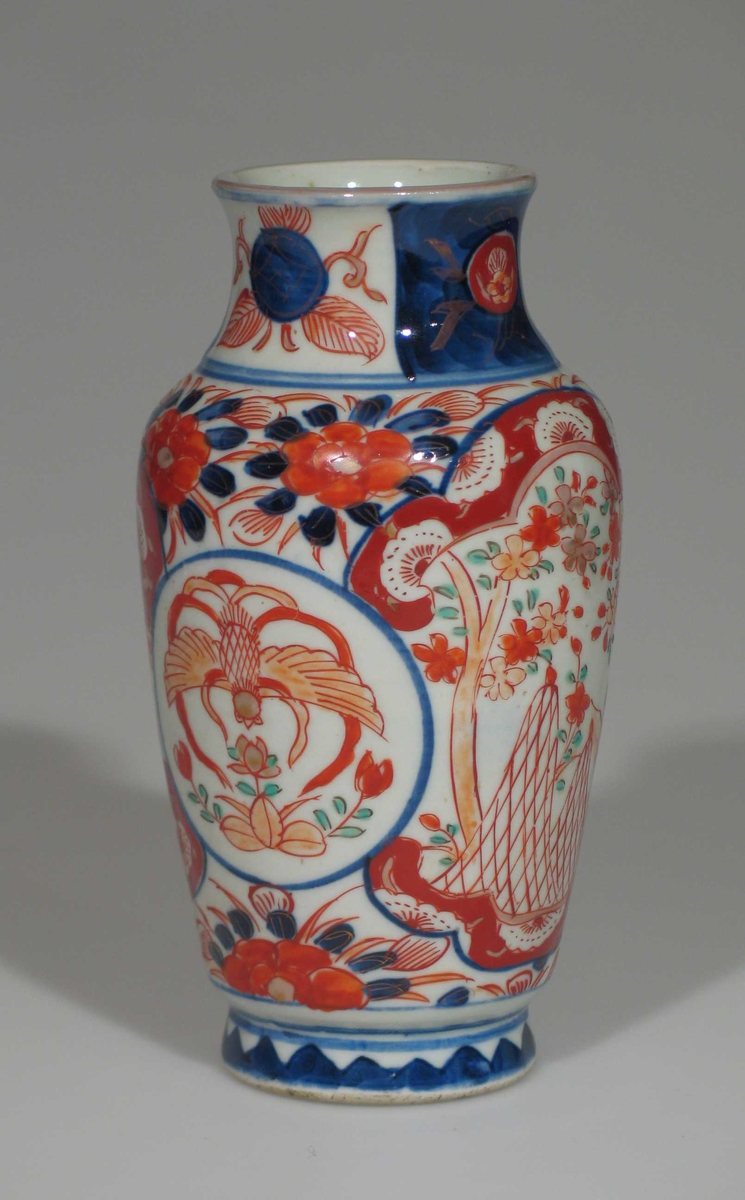 Hvit vase i porselen med dekor i blått og rustrødt. Vasen er urneformet.