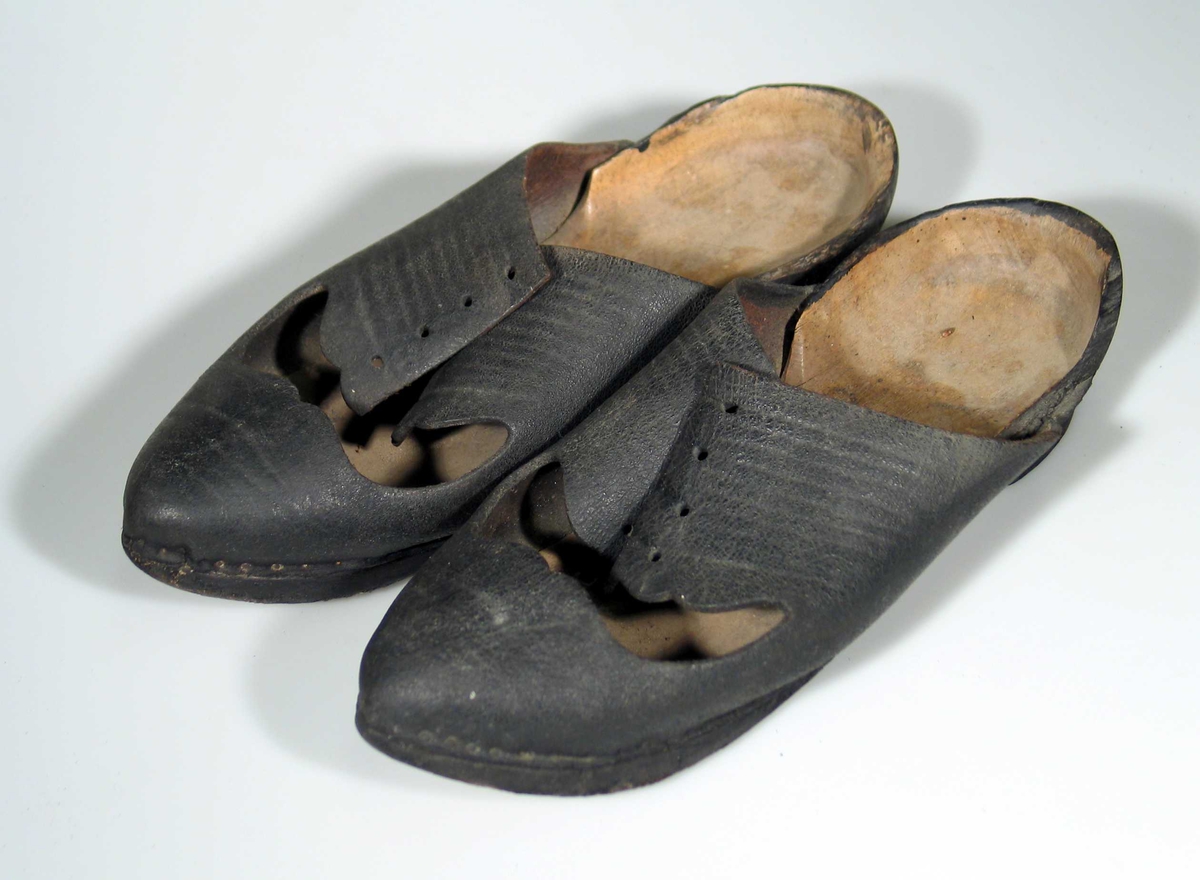 Sko med tresåle og svart overlær med hull for snøring. 
Hælen er i lær, men kan opprinnelig ha vært i tre.