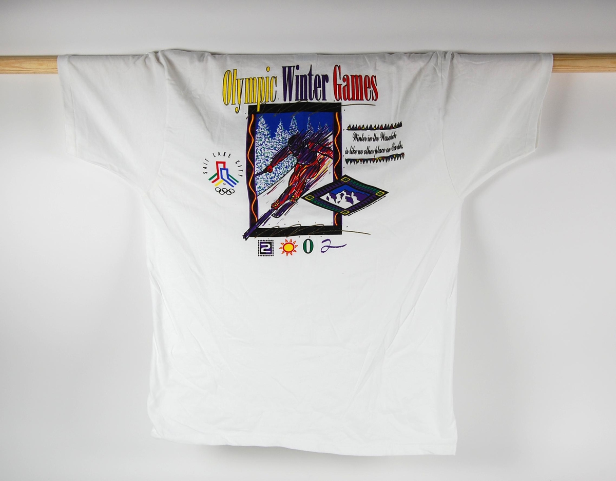 Hvit t-skjorte med flerfargede logoer og bilde av en alpinist. Det er blant annet logo for de olympiske leker i Salt Lake City i 2002. 