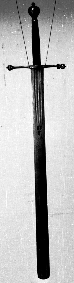 Skarprettersverd.  Pæreformet knapp med fasettetert dekor.
Tregrep viklet med rokkeskinn. 
Rette åttekantede parérstenger som ender i to dråper med kantet dekor. Rett tveegget klinge med ovalt tverrsnitt  og tre korte blodrender på hver side. Innslått tre smedstempler med kronede hoder.  På den ene siden er det gravert inn et hjul og på den andre siden en galge. Begge inngraveringer er innlagt med kobber.

