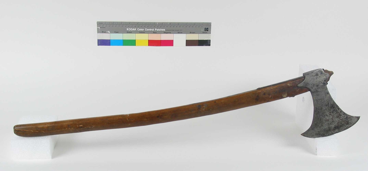 Symmetrisk blad. Bladet er tynt. 
Øsehammeren har skaftehull og fliker.
Etset dekor på begge sider. Stemplet TS på venstre side.
Gammelt treskaft med to orginale jernskinner med gravert dekor.
Jernskinnene er festet med nitter.