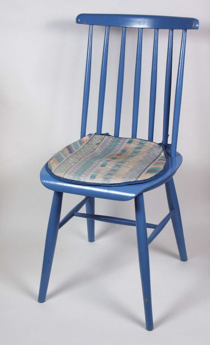 Blåmalt pinnestol i tre med mønstret pastellfarget pute.